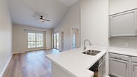 Located at 4804 Haverwood Lane in Dallas, TX, this 1-bedroom, 2-bathroom unit offers a well-designed layout with thoughtful finishes throughout. The open-concept living and kitchen area is immediately welcoming, featuring soaring vaulted ceilings that amplify the sense of space, wood-style plank flooring, and ceiling fans for year-round comfort. Large windows and a sliding glass door flood the living area with natural light and provide direct access to a private balcony with outdoor views.

The kitchen is equipped with a peninsula featuring a quartz countertop and a double stainless steel sink, gray cabinetry, black appliances including a range, microwave, and refrigerator. Built-in wall shelving in the living area adds functional character to the space.

The spacious primary bedroom includes vaulted ceilings, a ceiling fan, a sizeable closet with bi-fold doors, and an en-suite bathroom featuring a blue vanity with a window above. A second full bathroom with a tub-shower combo serves guests. Additional highlights include a dedicated laundry area and a closet for extra storage. Wood-style flooring runs consistently throughout, giving the entire unit a clean, cohesive aesthetic.