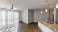 This single-story, 3-bedroom, 2-bathroom residence offers a thoughtfully designed open-concept layout with modern finishes throughout. The kitchen serves as the centerpiece of the living area, featuring dark espresso cabinetry, granite countertops, a mosaic tile backsplash, stainless steel appliances including a range, microwave, and dishwasher, and a large center island with a built-in sink and pendant lighting overhead. The kitchen flows seamlessly into the living area, which is bathed in natural light through floor-to-ceiling vertical blinds and sliding glass doors, and is accented by a ceiling fan. Wood-style flooring runs throughout the main living areas, complementing the contemporary aesthetic. The bedrooms are carpeted for comfort and include ceiling fans and window blinds. Both bathrooms maintain the same elevated design language, featuring granite-topped dark vanities and tub-shower combinations. The primary bathroom offers a dual-sink vanity with a large mirror. A dedicated laundry area houses a full-size washer and dryer with wire shelving above. Clean white walls, neutral tones, and consistent finishes create a cohesive, modern ambiance throughout this spacious residence.