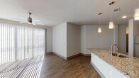 This single-story, 3-bedroom, 2-bathroom residence offers a thoughtfully designed open-concept layout with modern finishes throughout. The kitchen serves as the centerpiece of the living area, featuring dark espresso cabinetry, granite countertops, a mosaic tile backsplash, stainless steel appliances including a range, microwave, and dishwasher, and a large center island with a built-in sink and pendant lighting overhead. The kitchen flows seamlessly into the living area, which is bathed in natural light through floor-to-ceiling vertical blinds and sliding glass doors, and is accented by a ceiling fan. Wood-style flooring runs throughout the main living areas, complementing the contemporary aesthetic. The bedrooms are carpeted for comfort and include ceiling fans and window blinds. Both bathrooms maintain the same elevated design language, featuring granite-topped dark vanities and tub-shower combinations. The primary bathroom offers a dual-sink vanity with a large mirror. A dedicated laundry area houses a full-size washer and dryer with wire shelving above. Clean white walls, neutral tones, and consistent finishes create a cohesive, modern ambiance throughout this spacious residence.