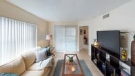 This single-floor residence offers a thoughtfully laid-out living space bathed in natural light throughout. The living room serves as the heart of the home, featuring light tile flooring, a textured ceiling, and large vertical-blind-covered windows and a sliding glass door that invite abundant natural light while offering outdoor access. The open flow connects seamlessly to a cozy dining nook, which includes built-in shelving and wall art, creating an intimate setting for everyday meals. The galley-style kitchen is efficiently designed with white cabinetry, light countertops, a double sink, a stovetop range, and a full-size refrigerator — providing ample functionality in a compact footprint. The bedroom is a restful retreat with tile flooring, soft neutral walls, and its own sliding glass door opening to an outdoor area with views of greenery and a pool, blending indoor comfort with outdoor accessibility. A dedicated workspace within the bedroom adds versatility to the room. The full bathroom is clean and straightforward, featuring a tub-shower combination, a vanity with storage, and tile flooring. Throughout the residence, the warm, neutral color palette and consistent tile flooring contribute to a cohesive and welcoming ambiance.
