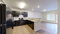This single-floor, two-bedroom, one-bathroom residence offers a thoughtfully designed layout that maximizes functionality. The open-concept kitchen and living area serves as the heart of the unit, where light wood-tone vinyl plank flooring runs throughout, creating a clean, cohesive look. The kitchen is well-equipped with dark espresso cabinetry, light granite-style countertops, black appliances including a full-size refrigerator, range, and dishwasher, and a peninsula that provides additional counter space and separates the kitchen from the living area. The living room receives natural light through a large window and sliding glass door, offering outdoor access.

The primary bedroom is generously sized and features plush carpeting, multiple electrical outlets, and a walk-in closet outfitted with wire shelving systems for organized storage. The second bedroom, also carpeted, includes a sliding-door closet with built-in wire shelving. The bathroom features a full tub-shower combination with tiled surround and wood-tone flooring. Neutral wall tones throughout give the space a clean, move-in-ready appearance.