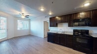 This single-floor unit offers a functional and cohesive layout designed for comfortable everyday living. The kitchen is a standout feature, showcasing rich dark espresso cabinetry that extends to the ceiling for ample storage, granite-style countertops, and a full suite of black appliances including a refrigerator, electric range, microwave, and dishwasher. Light wood-style flooring runs throughout the kitchen and main living areas, creating a warm, unified aesthetic that transitions seamlessly from room to room.

The open living area adjoins the kitchen, benefiting from natural light streaming through windows fitted with horizontal blinds. A ceiling fan overhead provides additional comfort and airflow. The layout connects directly to the bedroom, which features plush carpeting, a ceiling fan, a window with exterior views, and a sliding-door closet offering convenient storage.

The bathroom is clean and well-finished, featuring a dark vanity cabinet with granite-style countertop, a large mirror, wood-style flooring, and a full soaking tub with a tiled surround and built-in corner shelving. The entry area provides a practical transition point into the unit. Overall, the space presents a cohesive design with consistent finishes throughout.