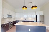 This elegant apartment, located in Residence BH, unit S2002, offers a generous 1500 square feet of living space on a single floor. The property boasts two bedrooms, including an impressively large primary bedroom of 1200 square feet, and two bathrooms. Floor-to-ceiling windows dominate the living areas, providing breathtaking panoramic views of the city skyline and surrounding landscape.

The interior is characterized by a modern, minimalist design with light-colored walls and sleek hardwood flooring throughout. The open-concept layout seamlessly connects the living, dining, and kitchen areas, creating an expansive feel. The kitchen features contemporary cabinetry and high-end appliances, complemented by pendant lighting.

Both bathrooms are finished to a high standard, with one showcasing luxurious marble tiling and a glass-enclosed shower. The apartment includes a well-designed closet space with built-in shelving and hanging areas for optimal organization.

Natural light floods the rooms, enhanced by the strategic use of roller shades for light control. The balcony offers an outdoor extension of the living space, perfect for enjoying the impressive urban views. This apartment combines spacious living with modern amenities in a prime high-rise setting.