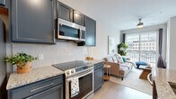 Located at 265 E State St in the heart of downtown Columbus, Ohio, this one-bedroom, one-bathroom unit offers a well-designed open-concept layout that maximizes every square foot. Light hardwood flooring flows throughout, creating a cohesive and bright aesthetic.

The kitchen is a standout feature, boasting slate-blue cabinetry, granite countertops, a herringbone tile backsplash, and a full suite of stainless steel appliances, including a refrigerator, electric range, and over-the-range microwave. A dark-toned island with bar seating provides additional prep space and a natural divide between the kitchen and living area.

The living room is bathed in natural light from large windows and a sliding glass door that opens to a private balcony overlooking the Columbus skyline — an ideal spot to take in the urban surroundings. A ceiling fan adds comfort to the space.

The bedroom features generous windows with city views, maintaining the same bright, airy feel found throughout the unit. The full bathroom is appointed with granite countertops, dark cabinetry with brushed nickel hardware, and a glass-enclosed shower. A dedicated in-unit laundry area with a stacked washer and dryer adds everyday convenience to this centrally located urban residence.