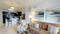 Located at 308 East 2nd Street in Hummelstown, Pennsylvania, this single-floor residence offers a thoughtfully designed open-concept layout that maximizes comfort and functionality. The living area serves as the heart of the home, featuring plush carpeted flooring, neutral-toned walls, and ample overhead ventilation. Large decorative wall art adds a touch of contemporary style, while a warm floor lamp enhances the inviting ambiance. The space comfortably accommodates stylish seating arrangements, making it well-suited for both relaxing and entertaining. A smooth visual flow connects the living area to the kitchen, which is outfitted with dark cabinetry, light-toned countertops, and pendant lighting that adds a modern accent. Bar-height seating at the counter creates a casual dining option that integrates naturally with the open layout. A doorway visible from the living area hints at additional private spaces within the residence. Throughout the home, the consistent use of neutral tones, clean lines, and practical design choices create a cohesive and welcoming atmosphere that balances everyday livability with modern aesthetic appeal.