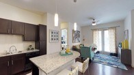 This single-floor residence offers a thoughtfully designed open-concept layout that seamlessly connects the kitchen, dining, and living areas. The kitchen is outfitted with rich dark espresso cabinetry, granite countertops, a tile backsplash, black appliances, and a double-basin sink. A curved granite breakfast bar with pendant lighting above serves as both a functional workspace and a natural divider between the kitchen and the dining area, which features hardwood-style flooring. The living area is bright and inviting, with a ceiling fan, sliding glass door access to the outdoors, and ample natural light. The dedicated dining space comfortably accommodates a full dining table and chairs. The bedrooms are carpeted and well-lit, each featuring ceiling fans and large windows that bring in generous natural light. The primary bedroom includes direct access to a spacious en-suite bathroom. The bathrooms are elegantly appointed with granite countertops, dual sinks, wide vanity mirrors with overhead lighting, a shower-tub combination, and walk-in closets with built-in shelving. Throughout the residence, warm neutral tones and consistent finishes create a cohesive and comfortable living environment.