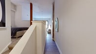 This one-bedroom, one-bathroom unit in Baltimore, MD offers a compelling blend of industrial character and modern finishes. The open floor plan makes smart use of the space, with the living, dining, and kitchen areas flowing seamlessly together. Soaring ceilings and large, grid-paned windows flood the living area with natural light, while exposed painted brick walls and structural columns add authentic loft-style character throughout.

The kitchen is a standout feature, outfitted with rich dark-wood cabinetry, granite countertops, and stainless steel appliances including a range, built-in microwave, and refrigerator. A peninsula with bar seating opens directly to the dining and living areas, making the space ideal for entertaining. Pendant lighting above the kitchen adds both function and style.

The living area is generously proportioned, offering room for a full seating arrangement and dining table beneath the dramatic ceiling height. Durable wood-look flooring runs throughout the main living spaces, complementing the unit's warm, contemporary aesthetic.

A hallway leads to the bedroom and bathroom, providing a sense of separation and privacy. The bathroom features matching dark wood cabinetry, a white vanity countertop, and a shower-tub combination with clean, neutral finishes. The overall design balances historic architectural elements with updated, modern amenities.