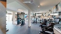 This fitness center in Oakland, CA, is a thoughtfully designed single-floor facility offering a generous, open workout environment. The space is defined by a striking, large-scale geometric mural that wraps around the walls, featuring an eye-catching palette of teal, gold, gray, and white angular shapes that lend a modern, energetic ambiance to the room.

The layout is divided into distinct functional zones. A cardio area houses multiple treadmills positioned near floor-to-ceiling sliding glass doors, which allow abundant natural light and provide views of the outdoor greenery. Adjacent to this zone, a cycling area features a row of stationary spin bikes equipped with digital displays, accompanied by wall-length mirrors that amplify the sense of space. A strength training zone includes a cable and pulley functional trainer, adjustable weight benches, and a full rack of dumbbells neatly organized for accessibility.

Ceiling fans are installed throughout, ensuring comfortable airflow during workouts. Recessed and track lighting supplements the natural light, maintaining a bright, motivating atmosphere. The flooring consists of durable rubber sport surfacing, appropriate for high-traffic fitness use. Wall-mounted flat-screen televisions are positioned for visibility across multiple workout zones, completing this well-appointed facility.