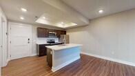 Located at 114 E Fifth Ave in Columbus, Ohio, this single-floor residence offers a thoughtfully designed open-concept layout that blends modern style with everyday functionality. The kitchen serves as the centerpiece of the living area, showcasing rich dark-espresso cabinetry, crisp white quartz countertops, and a full suite of stainless steel appliances including a refrigerator, electric range, microwave, and dishwasher. A spacious central island with an undermount sink provides additional prep space and doubles as a casual dining or entertaining hub. A distinctive tray ceiling with recessed lighting adds architectural depth and warmth to the kitchen and living area. Durable hardwood-style flooring flows throughout the main living spaces, lending a clean and cohesive aesthetic. The bedroom features plush carpeting and a bright window with blinds that frames views of the surrounding neighborhood, allowing for ample natural light. The bathroom is finished with a wood-look tile floor, dark vanity cabinetry with white countertops, and a glass-enclosed walk-in shower adorned with elegant marble-style tile surround. A private entry door and well-proportioned open floor plan round out this well-appointed Columbus residence.