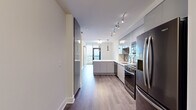 Located at 1400 W Peachtree St NW in Atlanta's Midtown neighborhood, this one-bedroom, one-bathroom unit offers a well-appointed layout with modern finishes throughout. The entrance opens into a galley-style kitchen that immediately impresses with high-gloss grey cabinetry extending to the ceiling, a grey subway tile backsplash, white quartz countertops, and a full suite of stainless steel appliances including a gas range, built-in microwave, dishwasher, and a large French door refrigerator. Track lighting overhead ensures the kitchen is well-illuminated. Rich hardwood-style flooring flows throughout the main living areas, adding warmth to the contemporary aesthetic. The bedroom is a serene retreat, featuring clean white walls, the same hardwood-style flooring, and a dramatic floor-to-ceiling window that frames sweeping views of the Atlanta skyline, filling the room with abundant natural light. A dedicated closet provides practical storage. The bathroom is finished with large-format light stone-look tile on both the floors and shower surround, complemented by a soaking tub, a grey vanity with a white countertop, and recessed lighting, creating a clean and calming atmosphere.