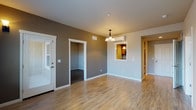 This single-floor residence offers a thoughtfully designed layout that balances living, sleeping, and utility spaces. The open living and dining area features warm-toned, hardwood-style laminate flooring and neutral gray walls, anchored by a decorative chandelier overhead. A wall-mounted mini-split unit provides supplemental climate control, while a pass-through window connects the space to the kitchen, enhancing the sense of openness.

The kitchen is equipped with stainless steel appliances, including a range, over-the-range microwave, and refrigerator. Warm wood cabinetry pairs with gray tile backsplash and ample counter space, creating a functional cooking environment.

The bedrooms are carpeted in a dark, neutral tone and receive natural light through large windows with views of surrounding greenery. The rooms offer generous wall space and are well-suited for comfortable furnishing arrangements.

A full bathroom features tile flooring, a full-sized soaking tub with shower, a wood-toned vanity, and clean white fixtures. A dedicated laundry closet with a stacked washer and dryer adds significant everyday convenience. The overall aesthetic is clean, modern, and move-in ready.