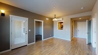This single-floor residence offers a thoughtfully designed layout that balances living, sleeping, and utility spaces. The open living and dining area features warm-toned, hardwood-style laminate flooring and neutral gray walls, anchored by a decorative chandelier overhead. A wall-mounted mini-split unit provides supplemental climate control, while a pass-through window connects the space to the kitchen, enhancing the sense of openness.

The kitchen is equipped with stainless steel appliances, including a range, over-the-range microwave, and refrigerator. Warm wood cabinetry pairs with gray tile backsplash and ample counter space, creating a functional cooking environment.

The bedrooms are carpeted in a dark, neutral tone and receive natural light through large windows with views of surrounding greenery. The rooms offer generous wall space and are well-suited for comfortable furnishing arrangements.

A full bathroom features tile flooring, a full-sized soaking tub with shower, a wood-toned vanity, and clean white fixtures. A dedicated laundry closet with a stacked washer and dryer adds significant everyday convenience. The overall aesthetic is clean, modern, and move-in ready.
