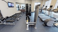 This fitness center is a thoughtfully designed, single-floor space built to accommodate a wide variety of exercise needs. The room features durable rubber flooring in a speckled blue-grey finish, providing both safety and comfort underfoot during workouts. Large windows allow natural light to fill the space, creating a bright and energizing atmosphere.

The strength training area is well-stocked, featuring a full rack of dumbbells in varying weights, flat workout benches, and a multi-functional cable machine ideal for a range of resistance exercises. A floor-to-ceiling mirror spans one wall, enhancing the sense of openness while allowing users to monitor their form during training.

The cardio section is equally impressive, lined with modern treadmills and an elliptical trainer, each equipped with individual screens for entertainment or performance tracking. Additional cardio equipment, including a stationary bike, rounds out the selection.

The space maintains a clean, contemporary aesthetic with neutral-toned walls and well-organized equipment placement that ensures ease of movement throughout. Wall-mounted monitors provide further convenience. Overall, the fitness center strikes a balance between functional layout and modern design, making it a practical and inviting environment for users of all fitness levels.