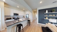 Located at 5811 102nd Street in Lubbock, Texas, this single-story home offers a well-designed, open-concept layout with modern finishes throughout. The kitchen serves as a central highlight, featuring crisp white cabinetry that extends to the ceiling for ample storage, dark countertops, and a full suite of stainless steel appliances including a French door refrigerator, microwave, and range. A peninsula with bar-top seating provides a casual dining option and creates a natural gathering space, seamlessly connecting the kitchen to the living areas. Recessed lighting illuminates the space with a clean, contemporary feel. Light hardwood-style flooring runs throughout, adding warmth and continuity across the open floor plan. A neutral color palette of whites and soft grays is complemented by a bold slate-blue accent wall near the entryway, adding a modern, stylish touch. A bright hallway leads to the remaining areas of the home, with natural light contributing to an airy atmosphere. The overall design balances functional layout with thoughtful aesthetic details, making it a comfortable and visually appealing single-floor residence.