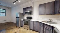 Located at 701 E Second St N in Wichita, Kansas, this one-bedroom, one-bathroom urban loft blends industrial character with modern upgrades. Polished concrete floors run throughout the entire space, reflecting light and reinforcing the loft's industrial-chic aesthetic. Exposed ceiling infrastructure, track lighting, and painted concrete block walls give the unit a distinct warehouse-inspired character.

The kitchen is a standout feature, outfitted with dark gray shaker-style cabinetry, marble-look quartz countertops, and a full suite of stainless steel appliances including a refrigerator, electric range, over-the-range microwave, and dishwasher. A stacked washer and dryer unit is conveniently integrated near the kitchen area.

The bedroom is a generously sized room, occupying roughly half the total floor area. It features painted brick accent walls, a closet, and large windows with blinds that allow natural light to fill the space while offering views of the surrounding neighborhood.

The bathroom offers a clean, modern design with a frameless glass walk-in shower, polished concrete flooring, and overhead cabinetry for storage. The overall ambiance of this loft is urban and functional, making efficient use of its compact footprint while delivering a stylish living environment in the heart of Wichita.