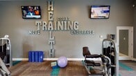 Located at 9610 Stoney Glen Dr in Mint Hill, NC, this well-appointed fitness center offers a comprehensive workout environment designed to support a variety of exercise routines. The single-floor space is finished with a combination of hardwood-style flooring and patterned carpet tiles accented in teal, adding a modern, energetic aesthetic throughout.

The main workout area is equipped with multiple cable and resistance machines, including a multi-station cable system and a variety of weight machines suited for both upper and lower body training. A full dumbbell rack provides a wide range of free weight options for strength training. Dual wall-mounted flat-screen televisions keep members entertained during workouts.

A dedicated functional training area features a power tower for bodyweight exercises, stability and medicine balls on a tiered rack, and yoga mats, making it ideal for stretching, core work, and flexibility training. Motivational wall lettering emphasizing health, training, goals, and endurance adds an inspiring touch to the space.

Natural light streams in through multiple sets of white-framed French doors, creating a bright and welcoming atmosphere. Crown molding, recessed lighting, and a ceiling fan contribute to the clean, polished finish of the space. The layout is open and spacious, allowing for comfortable movement between equipment stations.