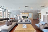 Located at 7400 Parkwood Ct in Falls Church, Virginia, this single-floor community lounge is a generously sized, open-plan space designed for comfort and social engagement. Rich hardwood flooring flows throughout, anchoring the modern aesthetic and tying together the various functional zones within the room.

The living area is thoughtfully appointed with contemporary seating, including plush sofas and accent chairs, arranged around a striking built-in fireplace set against a textured stone accent wall with warm wood detailing — a clear focal point of the space. Adjacent to this seating area, a large flat-screen television is mounted against a bold slate-blue accent wall, creating an inviting media lounge atmosphere.

A fully equipped kitchenette occupies one end of the space, outfitted with stainless steel appliances, dark cabinetry, and ample counter space, making the lounge well-suited for gatherings and events. A game area featuring a shuffleboard table adds a recreational dimension to the room.

Floor-to-ceiling windows along one wall flood the interior with abundant natural light while offering panoramic views of a resort-style outdoor pool and landscaped surroundings. Built-in banquette seating with cafe-style tables lines this window wall, providing a bright, relaxed nook. The overall ambiance is modern, welcoming, and versatile.