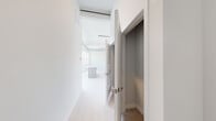This thoughtfully designed single-floor unit combines industrial loft character with modern, clean aesthetics. Light wood flooring runs continuously throughout the space, contributing to a cohesive and airy feel. The main living and kitchen area is expansive and open, highlighted by large multi-pane windows that flood the space with natural light and offer pleasant outdoor views of greenery and open sky. Exposed cylindrical ductwork runs along the ceiling, adding an industrial design element that contrasts elegantly with the crisp white walls and clean finishes. The kitchen features a central island with a light countertop and wood-toned cabinetry, alongside full-size appliances. The private rooms are well-proportioned with tall ceilings, clean white walls, and access to dedicated closet or storage spaces. Louvered closet doors and panel-style doors add subtle architectural detail throughout. A bathroom is finished with marble-style tile flooring, a wood-toned vanity with brushed nickel hardware, a rectangular mirror, and stylish globe lighting. A walk-in closet provides additional storage with warm-toned flooring. Throughout the unit, the palette remains bright and neutral, creating a versatile canvas well-suited to a variety of uses and design preferences.