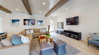 Located at 3215 Midvale Dr in Wilmington, NC, this single-floor space delivers a cohesive coastal aesthetic through thoughtful design and high-quality finishes. The main lounge area is anchored by shiplap-clad walls, exposed wood ceiling beams, and light hardwood-style flooring that creates an airy, relaxed atmosphere. A large sectional sofa, upholstered ottomans, and a wall-mounted TV make this an inviting gathering space, while glass doors provide direct views and access to an outdoor pool area, filling the room with natural light.

The kitchen and bar area is a standout feature, showcasing a generously sized island with X-detail accents in a coastal blue finish, topped with white countertops and lined with woven bar seating. Three matte black pendant lights hang overhead, complementing the aqua glass tile backsplash and white cabinetry. A wall-mounted TV adds functionality to this social hub.

Adjacent to the main areas, a dedicated office space offers a calmer, more neutral environment. Soft beige tones, textured wallcovering, and plush carpeting set a focused, professional tone. A sleek floating desk, ergonomic seating, and ample natural light from large windows make it a practical and comfortable workspace. Coastal-themed artwork and nautical décor details throughout tie the entire space together in a harmonious, seaside-inspired design.