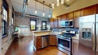 Located in the heart of downtown Buffalo on Main Street, this 1-bedroom, 1-bathroom loft-style residence masterfully blends industrial character with modern finishes. Exposed brick walls are a defining feature throughout, lending warmth and historic charm to every room. Rich hardwood floors run continuously across the space, complementing the building's urban aesthetic.

The open-concept living and dining area is anchored by floor-to-ceiling exposed brick, large multi-pane windows that flood the space with natural light, and soaring ceilings with exposed ductwork that reinforce the loft's industrial identity. The well-appointed kitchen features warm wood cabinetry, granite countertops, a mosaic tile backsplash, stainless steel appliances including a gas range and dishwasher, and stylish pendant lighting hanging from the elevated ceiling. A peninsula with bar seating offers a casual dining option.

A long hallway with exposed brick walls and exposed metal ductwork overhead connects the main living areas to the private bedroom. The bedroom offers high ceilings, a ceiling fan, hardwood floors, and a horizontal window that brings in natural light. The bathroom includes a granite-topped vanity, tile flooring, and access to the hallway. Additional practical spaces include a dedicated laundry room, utility room, and closet, making this a fully functional urban retreat.