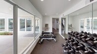 Located at 8787 Hammerly Blvd in Houston, Texas, this single-floor fitness center is thoughtfully designed to support a wide range of workout routines. The space is finished with durable rubber flooring and bathed in natural light through expansive floor-to-ceiling sliding glass windows and doors that open to views of the outdoor pool and surrounding community grounds, creating an energizing and open atmosphere.

The main workout area features a comprehensive dumbbell rack stocked with a full range of free weights, multiple adjustable workout benches, and full-length wall mirrors that enhance the sense of space and allow exercisers to monitor their form. A dedicated functional training zone is equipped with a well-organized rack holding an assortment of stability balls in multiple sizes, resistance bands, medicine balls, and yoga mats, supporting stretching, balance, and core training.

The space also includes a built-in water fountain and bottle-filling station conveniently located near the entrance, ensuring easy access to hydration. Recessed ceiling lighting supplements the abundant natural light throughout. A connecting corridor with tile flooring leads to additional facilities, completing a clean and functional layout designed with user convenience and comfort in mind.