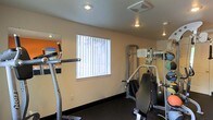 This single-floor fitness room is designed to provide a functional and efficient workout environment. The space is outfitted with a selection of exercise equipment, including a cardio machine and a multi-function strength training station, catering to a range of workout routines. The dark flooring provides a sturdy, slip-resistant surface well-suited for physical activity.

Natural light filters into the room through a window dressed with vertical blinds, offering both brightness and privacy control. Recessed and overhead lighting fixtures ensure the space remains well-lit at all hours. A wall-mounted mirror extends along one side of the room, creating a sense of added depth while allowing users to monitor their form during exercise.

The walls are finished in a neutral tone, with an accent wall featuring a bold orange detail that adds a touch of energy to the space. The overall layout is efficient, making practical use of the available area to accommodate multiple pieces of equipment without feeling cluttered. This fitness room serves as a convenient, self-contained space for maintaining an active lifestyle.