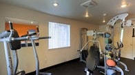 This single-floor fitness room is designed to provide a functional and efficient workout environment. The space is outfitted with a selection of exercise equipment, including a cardio machine and a multi-function strength training station, catering to a range of workout routines. The dark flooring provides a sturdy, slip-resistant surface well-suited for physical activity.

Natural light filters into the room through a window dressed with vertical blinds, offering both brightness and privacy control. Recessed and overhead lighting fixtures ensure the space remains well-lit at all hours. A wall-mounted mirror extends along one side of the room, creating a sense of added depth while allowing users to monitor their form during exercise.

The walls are finished in a neutral tone, with an accent wall featuring a bold orange detail that adds a touch of energy to the space. The overall layout is efficient, making practical use of the available area to accommodate multiple pieces of equipment without feeling cluttered. This fitness room serves as a convenient, self-contained space for maintaining an active lifestyle.