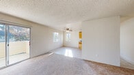 This single-floor residential unit offers a well-organized layout designed for comfortable everyday living. The spacious living room is a standout feature, bathed in natural light streaming through multiple windows and a large sliding glass door that opens to a private balcony with outdoor views. A ceiling fan adds comfort to the open area, while neutral-toned carpet flooring and a textured ceiling contribute to the room's clean, understated aesthetic.

Adjacent to the living area, the galley-style kitchen is outfitted with warm honey-toned wood cabinetry lining both sides, providing ample storage space. Light countertops, a double-basin sink, and white appliances including a range and refrigerator complete the functional setup, all set on easy-care tile flooring.

The bedrooms are carpeted and generously sized, offering practical closet solutions including a mirrored sliding-door closet that enhances the sense of space. One bedroom features dual closet doors for added storage versatility.

Two full bathrooms serve the unit, each finished with tile flooring, wood-toned vanity cabinetry, white countertops, and a tub-shower combination. The consistent use of neutral tones and warm wood accents throughout creates a cohesive and welcoming atmosphere across the entire unit.