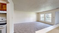 Located at 200 S Main St in Ellenville, New York, this single-floor unit offers a straightforward and functional layout designed for comfortable everyday living. The spacious living room is finished with neutral-toned wall-to-wall carpeting and a textured ceiling, and features a ceiling fan as well as windows that allow natural light to fill the space. A set of windows overlooks an outdoor balcony railing, providing a pleasant connection to the exterior. The living area flows openly toward a separate kitchen, which is accessible through a defined entryway. The galley-style kitchen is outfitted with warm wood-toned cabinetry, dark laminate countertops, a double-basin sink, and hardwood-style flooring. White appliances, including a refrigerator and electric range, complete the kitchen's functional setup. The bedroom is generously sized with soft carpeting, a window overlooking the surrounding grounds, and a built-in closet with bifold doors, offering ample storage. The bathroom features a full-size soaking tub with a shower combination and chrome fixtures, finished in clean white surrounds. Throughout the unit, neutral tones and a clean, move-in-ready condition create a calm and practical living environment well-suited for a variety of residents.