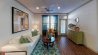 This 2-bedroom, 2-bathroom single-floor residence combines modern finishes with a functional layout designed for comfortable everyday living. The open-concept kitchen is a standout feature, showcasing dark espresso cabinetry, granite countertops, a mosaic tile backsplash, and stainless steel appliances including a range, microwave, and refrigerator. A large kitchen island with pendant lighting above provides additional prep space and casual seating for two. Rich hardwood-style flooring flows throughout the main living areas, adding warmth and continuity. The living room is bright and inviting, featuring crown molding, a ceiling fan, recessed lighting, and access to an exterior door framed by large windows that invite natural light. Both bedrooms are carpeted and include ceiling fans, large windows with natural light, and generous closet space. The primary bedroom connects to a spacious en-suite bathroom featuring dual sinks with granite countertops, dark cabinetry, and a tub-shower combination with tile surround. The second full bathroom mirrors the same refined finishes, with granite countertops and a tiled tub-shower. Throughout the residence, consistent design elements — granite surfaces, dark cabinetry hardware, and neutral tones — create a cohesive and polished aesthetic.