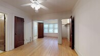 Located at 1007 N Cass St in Milwaukee's vibrant East Town neighborhood, this single-floor unit combines classic character with everyday functionality. The main living areas showcase warm, light-toned hardwood floors throughout, complemented by crown molding, crisp white walls, and ceiling fans that add both style and comfort. Dark-stained wood doors provide a rich contrast against the bright interior, lending a timeless charm to the space. The open layout flows naturally between rooms, with a windowed alcove at the far end of the living area that draws in natural light. A dedicated closet with built-in shelving offers practical storage. The kitchen is equipped with a gas range and a full-size refrigerator, finished with tile flooring and a window for ventilation and light. The bathroom retains its vintage appeal with classic pink wall tiles accented by black tile trim, a full soaking tub with overhead shower, a pedestal sink, a mirrored medicine cabinet, and a traditional penny-tile floor — all period-appropriate details that give the space a distinctive, enduring character. The overall ambiance is cozy and classic, well-suited for those who appreciate the architectural integrity of Milwaukee's historic residential buildings.