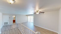 This single-floor unit offers a thoughtfully designed split-level layout, with a distinctive raised entry area framed by white-railed stairs that flows into a spacious open living area. Light hardwood-style flooring runs consistently throughout, lending a clean and cohesive feel to the space. The living area is generously sized, anchored by a ceiling fan with a light fixture and a large sliding glass door fitted with vertical blinds, allowing ample natural light and outdoor views to fill the room. An additional room with its own large sliding glass window also benefits from natural light and garden views, making it well-suited as a bedroom or flex space. A second bedroom features a similarly sized window and a closet, offering a practical and airy retreat. The galley-style kitchen is efficiently laid out with warm wood cabinetry, dark countertops, a stainless steel sink, and black appliances, including a gas range and refrigerator, with a window above that brings in natural light. The full bathroom is neatly appointed with a tiled shower-tub combination, a vanity with a wood cabinet base, and a large mirror. Clean neutral tones and consistent flooring throughout the unit create a bright, unified aesthetic.