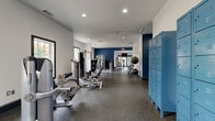 The Dutton fitness center at 1345 Wenlon Dr in Murfreesboro, Tennessee is a generously sized, single-floor exercise facility designed to support a comprehensive workout experience. The space is thoughtfully organized into distinct training zones, each clearly defined by bold navy blue accent walls, crisp white finishes, and durable rubber flooring throughout.

The strength training area is prominently labeled and features a full rack of dumbbells, cable machines, and Hoist multi-function strength equipment, complemented by functional training tools such as a heavy tire for conditioning work. A dedicated cardio zone houses a row of modern Matrix and Precor machines — including treadmills, ellipticals, stair climbers, and stationary bikes — each equipped with individual display screens. Full-length mirrors line portions of the walls, amplifying the sense of space and allowing users to monitor their form.

Natural light filters in through multiple arched and rectangular windows, keeping the environment bright and energizing. Recessed ceiling lighting provides consistent illumination throughout. Blue steel lockers offer convenient storage near the entrance, while water access and restroom facilities are available within the space. A large branded mural wall adds a dynamic, motivational aesthetic to the interior. The overall design balances a modern, professional gym atmosphere with a welcoming, community-oriented feel.