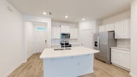 This two-story home presents a bright, clean aesthetic defined by crisp white walls, light wood-look flooring, and recessed lighting throughout. The entry foyer welcomes guests through a six-panel door accented by a transom window above, immediately opening to a spacious living area. A staircase with a dark wood banister and metal balusters connects the two floors, adding a subtle architectural contrast to the otherwise light interior.

The open-concept kitchen serves as a central hub, anchored by a large island featuring a white quartz countertop and an undermount double sink with a modern pull-down faucet. White shaker-style cabinetry lines the walls, complemented by a subway tile backsplash and a full suite of stainless steel appliances, including a French door refrigerator with ice and water dispenser, electric range, and over-the-range microwave. A dedicated laundry room houses a full-size washer and dryer with a louvered storage door nearby.

Bedrooms are well-proportioned, each featuring ceiling fans, natural light from double windows, and ample closet space. The bathroom includes white vanity cabinetry, a single-basin sink, and a three-bulb vanity light fixture. Throughout, the home maintains a cohesive, move-in-ready feel.