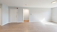 Located at 134 College Hwy in Southampton, Massachusetts, this two-bedroom apartment offers a thoughtfully arranged single-floor layout. Light wood-style flooring runs consistently throughout, lending a clean, cohesive feel to every room. The combined kitchen and living area serves as the heart of the unit, with the kitchen showcasing two-toned cabinetry — white upper cabinets paired with soft blue lower cabinets — complemented by a stone-look backsplash, stainless steel appliances including a refrigerator and dishwasher, and a window above the sink that allows natural light to filter in. The living room area is bright and open, with large windows and baseboard heating. Both bedrooms feature a distinctive grid-patterned accent wall, light flooring, and ceiling-mounted light fixtures. The primary bedroom is generously sized and includes a built-in closet with gold hardware. A hallway connects the main living spaces to the bedrooms, providing a clear and functional flow throughout the unit. The entrance opens directly into the living area, completing a straightforward and practical floor plan suited for comfortable everyday living.