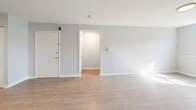 Located at 134 College Hwy in Southampton, Massachusetts, this two-bedroom apartment offers a thoughtfully arranged single-floor layout. Light wood-style flooring runs consistently throughout, lending a clean, cohesive feel to every room. The combined kitchen and living area serves as the heart of the unit, with the kitchen showcasing two-toned cabinetry — white upper cabinets paired with soft blue lower cabinets — complemented by a stone-look backsplash, stainless steel appliances including a refrigerator and dishwasher, and a window above the sink that allows natural light to filter in. The living room area is bright and open, with large windows and baseboard heating. Both bedrooms feature a distinctive grid-patterned accent wall, light flooring, and ceiling-mounted light fixtures. The primary bedroom is generously sized and includes a built-in closet with gold hardware. A hallway connects the main living spaces to the bedrooms, providing a clear and functional flow throughout the unit. The entrance opens directly into the living area, completing a straightforward and practical floor plan suited for comfortable everyday living.