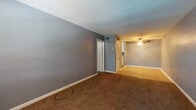 This single-floor unit offers a straightforward and functional layout designed to maximize the available space. The living area features warm brown carpeting, cool gray walls, and a textured ceiling, creating a neutral backdrop adaptable to various furnishing styles. A ceiling fan provides overhead lighting and air circulation, while closet doors and a visible entryway to the kitchen add practical convenience. The space transitions naturally into a dining or secondary living area, also finished with tile flooring leading into the kitchen.

The galley-style kitchen is efficiently organized, with white cabinetry lining both sides from floor to ceiling, providing generous storage. White appliances — including a range, refrigerator, and dishwasher — are neatly integrated alongside a double-basin sink and laminate countertops. Tile flooring runs throughout the kitchen, offering easy maintenance.

The bedroom continues the gray color palette with plush brown carpet, a window allowing natural light, a textured ceiling with flush-mount lighting, and direct access to a closet. The bathroom features a single vanity with a speckled countertop, an undermount sink, and a large mirror, keeping the space bright and clean. Overall, the unit presents a cohesive, move-in ready environment.