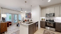 Located at 1888 Brittmoore Rd in Houston, TX, this one-bedroom, one-bathroom residence offers a thoughtfully designed single-floor layout that maximizes every square foot. The open-concept living and kitchen area creates a seamless flow, anchored by a central kitchen island with granite countertops and a stainless steel sink. The kitchen is well-equipped with two-tone cabinetry — warm wood lower cabinets paired with light upper cabinets — complemented by a classic subway tile backsplash and a full suite of stainless steel appliances, including a refrigerator with ice maker, range, microwave, and dishwasher. Light wood-style flooring runs throughout, adding warmth and continuity to the space. The living room is bright and inviting, featuring a ceiling fan and a glass sliding door that opens to a private balcony, allowing natural light to fill the room. The spacious primary bedroom includes a closet and connects to the well-appointed bathroom, which features granite countertops, ample cabinetry, and clean, neutral finishes. A dedicated laundry area with a washer and dryer is also conveniently accessible. Clean white walls and modern fixtures throughout give the space a fresh, contemporary feel.