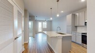 This single-floor residence is designed with a contemporary, open-concept layout that seamlessly connects the kitchen and living areas. The kitchen serves as a central highlight, featuring granite countertop surfaces, gray shaker-style cabinetry, and a full suite of stainless steel appliances, including a refrigerator, range, microwave, and dishwasher. A large kitchen island with an integrated sink and pendant lighting above adds both functionality and visual appeal. Light wood-style flooring runs throughout the main living areas, complementing the neutral gray and beige wall tones.

The living area is generously proportioned, with a ceiling fan and a glass door providing direct access to a balcony, allowing natural light to fill the space. Bedrooms are carpeted for comfort, with one room featuring a built-in granite-topped desk with drawers, offering a practical workspace. The bathroom is well-appointed with a tub-shower combination, a granite vanity with an undermount sink, a large mirror, and matching light wood-style flooring. Throughout the unit, clean lines, recessed lighting, and consistent finishes create a cohesive, modern ambiance.