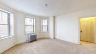 Located at 7427 S South Shore Dr in Chicago's South Shore neighborhood, this single-floor unit offers a straightforward and functional layout with a warm, classic character. The living area is generously proportioned, featuring soft wall-to-wall carpeting, crisp white walls, and a textured ceiling. A distinctive bay window arrangement floods the room with natural light and provides views of the surrounding neighborhood, while a traditional cast-iron radiator underscores the building's timeless architectural roots.

The kitchen is efficiently designed with warm honey-toned wood cabinetry extending to the upper walls, light granite-style countertops, and wood-look vinyl flooring. It is equipped with a gas range, refrigerator, and a stainless steel sink beneath a window, creating a bright and practical cooking space. The kitchen opens directly toward the main living area, enhancing the sense of connectivity throughout the unit.

Additional carpeted rooms offer flexible use as bedrooms or living spaces, each with natural light from single windows and clean white walls. The full bathroom includes a tub-shower combination, a vanity with sink, a toilet, and a window for ventilation, finished with tile flooring. Radiator heating is present in multiple rooms, reflecting the building's classic Chicago construction. The overall ambiance is clean, functional, and ready for personalization.