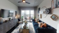 This contemporary single-floor residence showcases a thoughtfully designed open-concept layout that seamlessly connects the kitchen, dining, and living areas. The kitchen is a standout feature, outfitted with sleek gray cabinetry, stainless steel appliances, a light-colored tile backsplash, dark hardwood flooring, and a generously sized island with bar seating — ideal for both everyday living and entertaining. The living room is bright and inviting, featuring an exposed concrete ceiling, a ceiling fan, and floor-to-ceiling sliding glass doors that open to a balcony with sweeping city views. Eclectic wall décor and a tufted navy sofa add a sophisticated, urban character to the space. The primary bedroom is serene and well-proportioned, with large windows that bring in abundant natural light and views of the surrounding cityscape, complemented by soft carpet flooring and an exposed concrete ceiling. The en-suite primary bathroom features dual granite-topped vanities, gray cabinetry, large-format tile flooring, and access to a walk-in closet. A second bedroom offers similar comfort and natural light, while the secondary bathroom provides a full tub-shower combination, granite countertops, and matching gray cabinetry, maintaining a consistent, polished aesthetic throughout the residence.