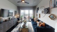 This contemporary single-floor residence showcases a thoughtfully designed open-concept layout that seamlessly connects the kitchen, dining, and living areas. The kitchen is a standout feature, outfitted with sleek gray cabinetry, stainless steel appliances, a light-colored tile backsplash, dark hardwood flooring, and a generously sized island with bar seating — ideal for both everyday living and entertaining. The living room is bright and inviting, featuring an exposed concrete ceiling, a ceiling fan, and floor-to-ceiling sliding glass doors that open to a balcony with sweeping city views. Eclectic wall décor and a tufted navy sofa add a sophisticated, urban character to the space. The primary bedroom is serene and well-proportioned, with large windows that bring in abundant natural light and views of the surrounding cityscape, complemented by soft carpet flooring and an exposed concrete ceiling. The en-suite primary bathroom features dual granite-topped vanities, gray cabinetry, large-format tile flooring, and access to a walk-in closet. A second bedroom offers similar comfort and natural light, while the secondary bathroom provides a full tub-shower combination, granite countertops, and matching gray cabinetry, maintaining a consistent, polished aesthetic throughout the residence.