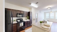 Located at 4250 Old Decatur Rd in Fort Worth, TX, this single-level residence offers a practical and comfortable layout featuring two bedrooms and two full bathrooms. The kitchen is a standout feature, showcasing rich dark-wood cabinetry extending to the ceiling for ample storage, light-toned countertops, a breakfast bar with a built-in sink, and black appliances including a refrigerator, electric range, and over-the-range microwave. Hardwood-style flooring runs through the kitchen and living areas, lending warmth and continuity throughout the main spaces. The living room benefits from natural light via a glass-paneled entry door and offers a clean, open feel. Both bedrooms are finished with plush carpet and ceiling fans, providing a cozy atmosphere. The primary bedroom includes direct access to a dedicated bathroom and a closet. The secondary bedroom also features a ceiling fan and a window for natural light. Each bathroom is outfitted with dark cabinetry and tiled surrounds. Two closets throughout the unit provide added storage convenience. The neutral color palette and clean finishes create a bright, move-in-ready environment suited for everyday living.