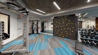 This well-appointed fitness center offers a comprehensive workout environment designed with both functionality and aesthetics in mind. The space is unified by striking patterned carpet tiles in grey and teal blue, which complement the modern interior throughout. The ceiling design incorporates a combination of wood-paneled insets, recessed troffers, and linear LED fixtures that provide bright, even illumination across all workout zones.

A standout feature is the dedicated "Freedom Climber" climbing wall, mounted on a textured dark panel and fitted with yellow handholds, offering a unique functional fitness option. Adjacent to this area, cable machines and multi-use strength equipment are arranged for efficient use of the space.

The free weights section features a fully stocked dumbbell rack and kettlebell storage along a dark accent wall, alongside a barbell weight tree and a cable resistance machine. A reclaimed wood accent column adds a warm, rustic contrast to the otherwise contemporary design.

The cardio zone houses stationary bikes positioned in front of a dramatic black-and-white vintage cycling mural, adding a creative visual focal point. Treadmills and ellipticals occupy a separate area near a glass door entry, which allows natural light in. A water fountain station and restroom access are conveniently located nearby.