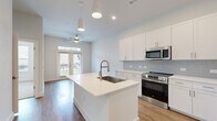This single-story unit in Stafford, Texas offers a thoughtfully designed open-concept layout that maximizes its compact footprint. The living and kitchen areas share a continuous, light-filled space anchored by warm hardwood-style flooring and crisp white walls. A ceiling fan enhances airflow in the living area, which features French doors that invite natural light and provide outdoor access.

The kitchen is a standout feature, boasting white shaker cabinetry extending to the ceiling for ample storage, a light gray subway tile backsplash, and stainless steel appliances including a range, microwave, and refrigerator. A central island with a white quartz countertop and an integrated sink with a brushed nickel pull-down faucet serves as both a prep area and gathering space. Pendant lighting above the island adds a polished finishing touch.

The bedroom is a comfortable, quiet retreat finished with plush neutral carpet and direct access to a dedicated closet. The bathroom features a white vanity with quartz countertops, upper storage cabinets, wood-style flooring, and a marble-tiled walk-in shower, combining functionality with a clean, modern aesthetic throughout.