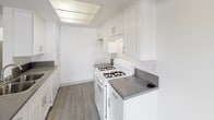 This single-floor unit offers a well-designed, open-concept layout that seamlessly connects the living area and kitchen, creating a bright and functional living space. Wood-look plank flooring runs throughout, providing a warm, cohesive aesthetic.

The kitchen is outfitted with white shaker-style cabinetry featuring brushed nickel hardware, dark countertops, a gas range, and a peninsula that opens toward the living area. Adjacent built-in cabinetry with matching countertop provides additional storage and counter space. A ceiling fan serves both the kitchen and the spacious living area, which is further brightened by large windows that invite natural light. A wall-mounted air conditioning unit offers supplemental climate control.

The bedrooms are bright and well-proportioned, each featuring large sliding windows and the same wood-look flooring. One bedroom includes a mirrored sliding-door closet, adding depth and light to the room, along with direct access to a full bathroom.

The bathroom is cleanly appointed with a white vanity with dark countertop, a wall-mounted mirror, and a tub-shower combination. A hallway connecting the rooms includes additional built-in storage and a tall utility unit. Textured ceilings are present throughout, and the overall palette of white walls and neutral tones gives the space a fresh, clean character.
