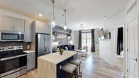 Located at 3100 S 7th St in St. Louis, MO, this single-floor unit showcases a thoughtfully designed open-concept layout that seamlessly connects the kitchen, dining, and living areas. Light hardwood flooring flows throughout the main living space, complemented by neutral gray walls and contemporary geometric pendant lighting that adds a striking visual element overhead.

The kitchen is outfitted with gray shaker-style cabinetry, stainless steel appliances, a chevron-patterned tile backsplash, and crisp white quartz countertops. A navy blue island with seating provides additional prep space and serves as a natural divider between the kitchen and living area.

The living room is anchored by a bold industrial mural spanning the full accent wall, creating an eye-catching focal point. A navy sofa, light gray armchairs, and a marble-topped coffee table furnish the space, while large windows dressed in dark curtains and Roman shades allow natural light to fill the room.

The bedrooms feature plush carpeting, textured accent walls, and generous windows with outdoor views. The bathroom is clean and functional, with subway tile surrounding the tub-shower combination, dark tile flooring, and a streamlined vanity.