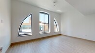 This thoughtfully designed single-floor unit blends contemporary finishes with distinctive architectural character. The standout feature of the main living area is a set of dramatic arched windows with bold black frames, flooding the space with abundant natural light and offering elevated views of the surrounding urban skyline. The soaring ceilings amplify the open, airy feel of the living space, which is finished with light-toned hardwood flooring throughout.

The kitchen is outfitted with crisp white cabinetry extending to the ceiling, warm-toned countertops, and a full suite of stainless steel appliances including a gas range, microwave, dishwasher, and refrigerator — providing both style and functionality.

The bedroom offers a quieter, cozier atmosphere, carpeted for comfort and featuring a double-door closet for ample storage. The bathroom is clean and modern, appointed with a wide vanity featuring an undermount sink, warm gold-toned fixtures, a medicine cabinet mirror, and a full soaking tub with shower. Light wood-look flooring ties the bathroom's aesthetic together seamlessly.

Throughout the unit, the white walls, natural light, and consistent material palette create a cohesive, inviting ambiance well-suited for urban living.