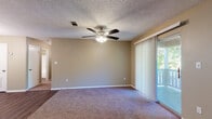 This single-story 2-bedroom, 2-bathroom residence offers a well-designed layout with a warm, neutral color palette and a blend of hard flooring and plush carpet throughout. The spacious living room serves as the heart of the home, featuring a corner fireplace with a classic white mantel, a ceiling fan with light fixture, and sliding glass doors with vertical blinds that open to a private balcony, allowing for an abundance of natural light and outdoor views. The transition from dark wood-style hard flooring in the entryway to soft carpeting in the main living area adds both visual interest and comfort underfoot. The kitchen is thoughtfully equipped with white raised-panel cabinetry, light stone-look countertops, dark wood-style flooring, and black appliances including an electric range with overhead ventilation. A pantry with bifold doors provides additional storage. Both bedrooms are carpeted and include ceiling fans, with the second bedroom featuring a window with blinds for natural light. A carpeted hallway connects the bedrooms to the rest of the home. The two bathrooms are finished with white cabinetry, stone-look countertops, wood-style flooring, and tub/shower combinations, with one bathroom also featuring a framed vanity mirror and wall sconce lighting.