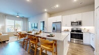 This single-floor residence is thoughtfully designed with a modern, open-concept layout that promotes a seamless flow between living spaces. The kitchen serves as a central hub, showcasing tall white shaker cabinetry, granite countertops, stainless steel appliances including a French door refrigerator, electric range, and built-in microwave. A generously sized island with bar seating provides additional prep space and casual dining options. Recessed lighting and under-cabinet illumination enhance the kitchen's bright, clean aesthetic.

The living area is anchored by large windows that invite natural light and features wood-look flooring and a ceiling fan overhead. The space connects directly to the bedrooms, creating an intuitive and functional floor plan. Each bedroom is well-proportioned with windows fitted with blinds and drapery. One bedroom includes direct access to a walk-in closet equipped with dual hanging rods and shelving, as well as an adjoining bathroom featuring granite countertops, white cabinetry with brushed nickel hardware, and a undermount sink. Wood-look flooring flows consistently throughout the residence, contributing to a cohesive, contemporary feel across all rooms.